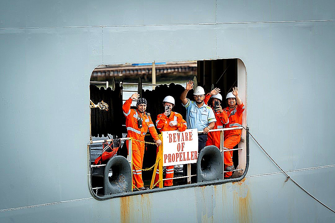 Crew members wave from a ship's opening.