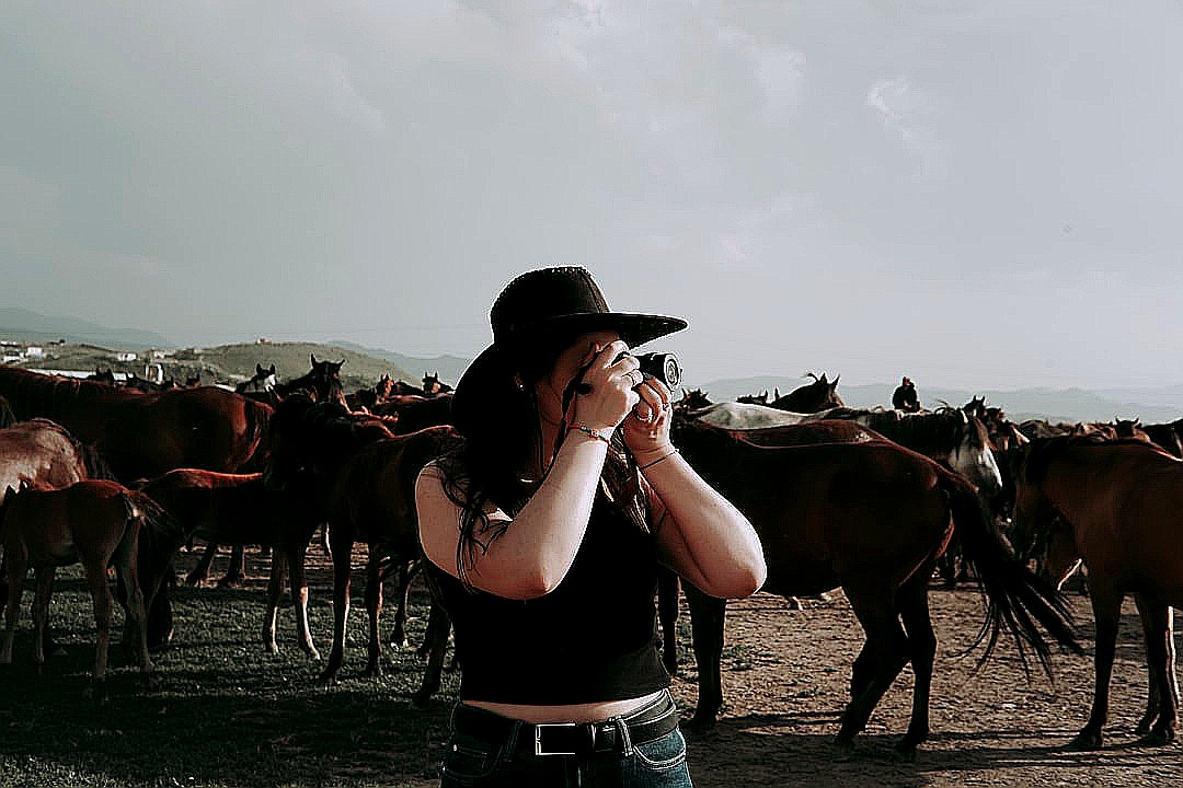 a woman taking a picture of a herd of horses
