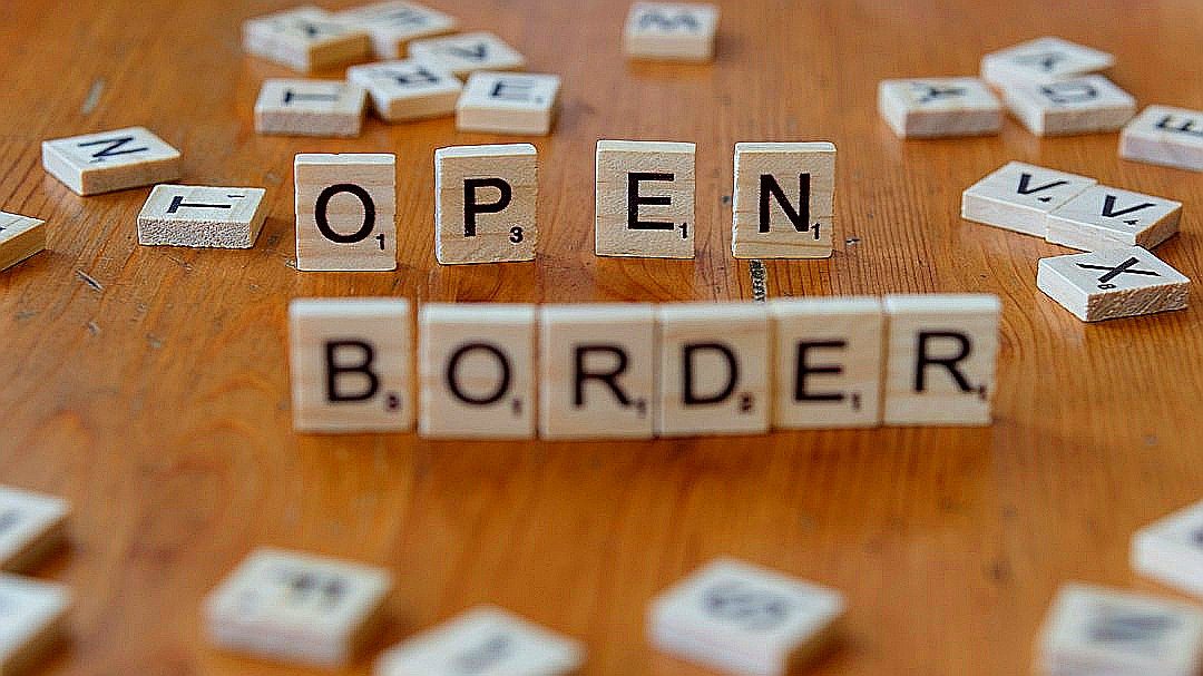 A wooden table topped with scrabble tiles spelling open border